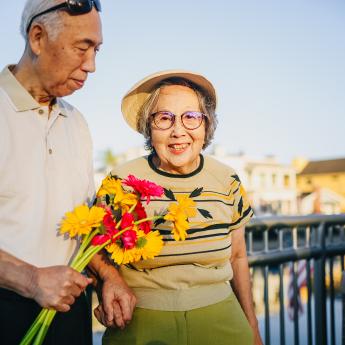 An Asian man holds flowers while an Asian woman looks at the camera.
