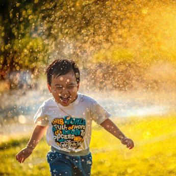 A child running through a sprinkler at sunset