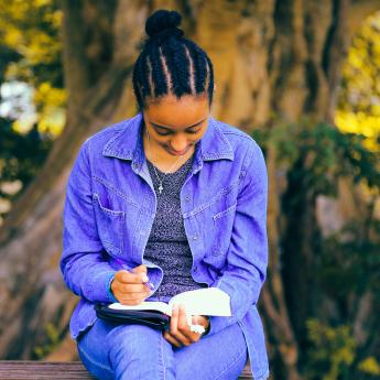 A Black woman with a purple shirt reads a book.